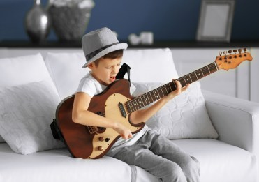Little boy playing guitar on a sofa at home