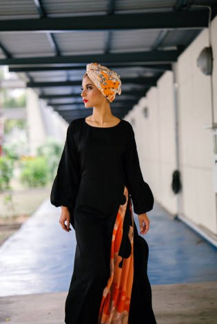 A stylish and fashionable Muslim Malay woman walks down a corridor during the day. She is wearing a colorful turban and a flowing and comfortable ethic garment.